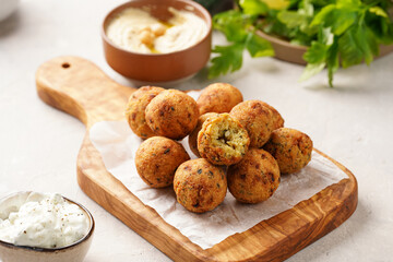 Traditional oriental chickpea deep fried falafel on a wooden board, tzatziki yoghurt sauce, hummus, fresh lime and green cilantro on light surface