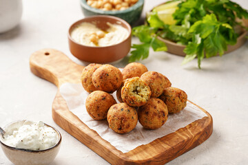 Traditional oriental chickpea deep fried falafel on a wooden board, tzatziki yoghurt sauce, hummus, fresh lime and green cilantro on light surface