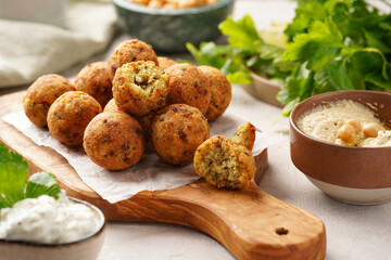 Traditional oriental chickpea deep fried falafel on a wooden board, tzatziki yoghurt sauce, hummus, lime and fresh green cilantro on light surface