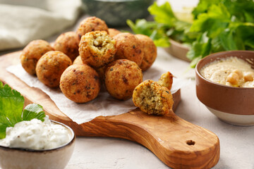 Traditional oriental chickpea deep fried falafel on a wooden board, tzatziki yoghurt sauce, hummus, fresh lime and green cilantro on light surface