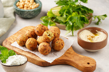 Traditional oriental chickpea deep fried falafel on a wooden board, tzatziki yoghurt sauce, hummus, fresh lime and green cilantro on light surface