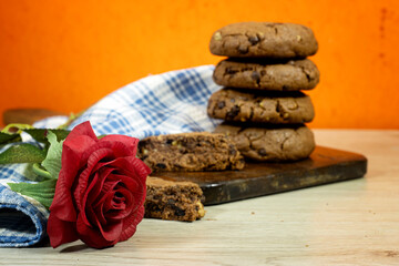 homemade chocolate cookies on wooden board, red rose flower on wood table