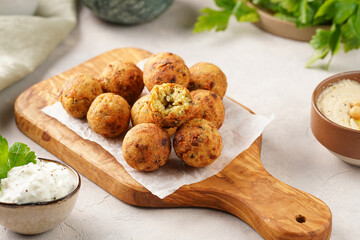 Traditional oriental chickpea deep fried falafel on a wooden board, tzatziki yoghurt sauce, hummus, fresh lime and green cilantro on light surface