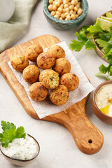 Traditional oriental chickpea deep fried falafel on a wooden board, tzatziki yoghurt sauce, hummus, fresh lime and green cilantro on light surface