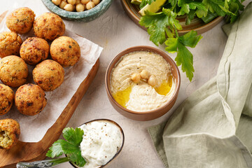 Traditional oriental chickpea deep fried falafel on a wooden board, tzatziki yoghurt sauce, hummus, fresh lime and green cilantro on light surface