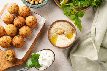 Traditional oriental chickpea deep fried falafel on a wooden board, tzatziki yoghurt sauce, hummus, fresh lime and green cilantro on light surface
