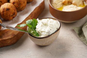 Traditional oriental chickpea deep fried falafel on a wooden board, tzatziki yoghurt sauce, hummus, fresh lime and green cilantro on light surface