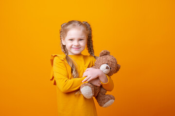 cute little girl holding a teddy bear on a yellow background, hugging