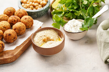Traditional oriental chickpea deep fried falafel on a wooden board, tzatziki yoghurt sauce, hummus, fresh lime and green cilantro on light surface