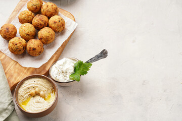Traditional oriental chickpea deep fried falafel on a wooden board, tzatziki yoghurt sauce, hummus, fresh lime and green cilantro on light surface, copy space for tet