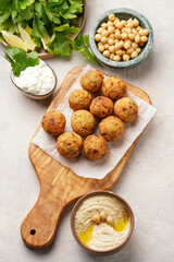 Traditional oriental chickpea deep fried falafel on a wooden board, tzatziki yoghurt sauce, hummus, fresh lime and green cilantro on light surface