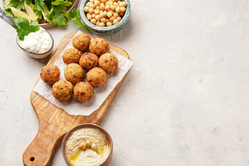 Traditional oriental chickpea deep fried falafel on a wooden board, tzatziki yoghurt sauce, hummus, fresh lime and green cilantro on light surface, copy space