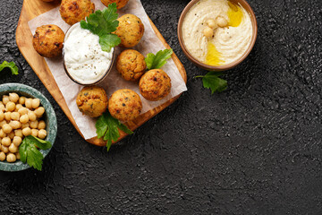 Traditional oriental chickpea deep fried falafel on a wooden board, tzatziki yoghurt sauce, hummus, fresh lime and green cilantro on black surface, copy space