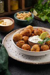 Traditional oriental chickpea deep fried falafel in a deep bowl with tzatziki yoghurt sauce, hummus, fresh lime and green cilantro on black surface