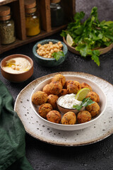 Traditional oriental chickpea deep fried falafel in a deep bowl with tzatziki yoghurt sauce, hummus, fresh lime and green cilantro on black surface