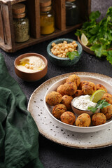 Traditional oriental chickpea deep fried falafel in a deep bowl with tzatziki yoghurt sauce, hummus, fresh lime and green cilantro on black surface