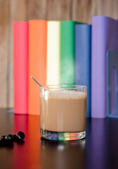 glass cup with hot latte on purple work desk, headphones and books with lgbt movement colors