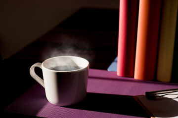 White ceramic mug with hot coffee on purple work desk and books with lgbt movement colors