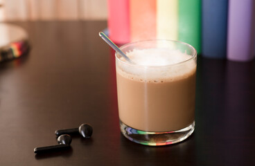 glass cup with hot latte on purple work desk, headphones and books with lgbt movement colors