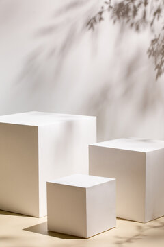 Abstract minimal nature scene - empty stage with three white rectangle podiums on beige background and shadows of tree leaves. Pedestal for cosmetic product and packaging mockups display presentation