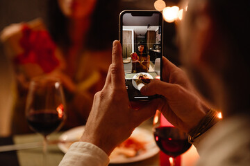 White man taking photo of his girlfriend during romantic dinner at home