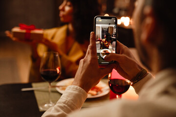 White man taking photo of his girlfriend during romantic dinner at home