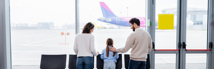 parents looking at daughter near window in airport, banner.