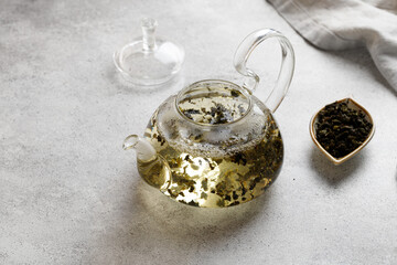 Teapot with green herbal tea leaves on a gray background on a table with a napkin. Hot teapot.