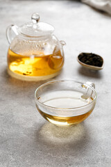 A mug or cup with green herbal tea and a teapot with tea leaves on grey background. Beauty color