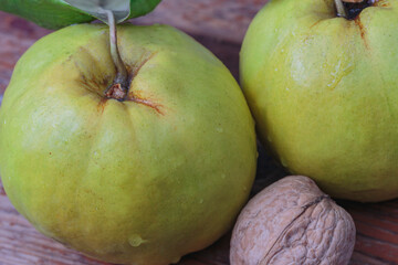 macro, two fresh quince with walnut on a wooden board, top view