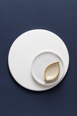 Ceramic plate and gravy boat on white round podium on blue background. Top view. Simple and minimalism.