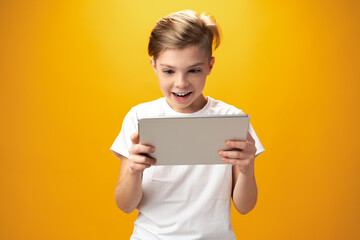 Little boy playing with digital tablet against yellow background