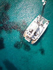 Bird's eye view of a white boat, swimming in the blue, shining sea under the sunlight and coastline