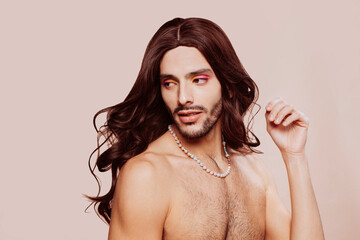 Portrait of drag queen posing, looking away, wearing eyeshadow, necklace and wig at studio over beige background. Beauty, make-up and skin care concept. Copy space.