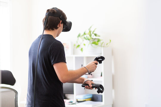 Young man playing game with virtual reality technology inside home