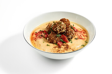 Hummus with olive oil, tomatoes and specials in a bowl on a white plate. Photo for the menu. Isolated