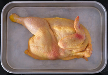 Halved uncooked chicken laid in a roasting tin rady for the oven - obrazy, fototapety, plakaty