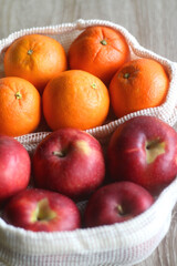 Two sustainable shopping bags filled with apples and oranges on wooden table. Selective focus.