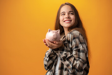Teen girl with piggy bank on yellow background.
