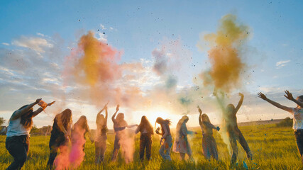 Cheerful girls toss up multi-colored powder at a beautiful sunset.