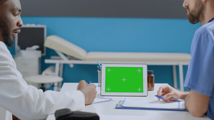 Multi-ethnic team of specialist analyzing medication treatment report discussing medical expertise. Mock up green screen chroma key horizontal tablet computer with isolated display in hospital offiice