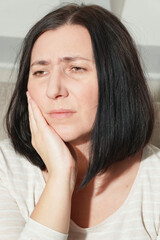 Middle age mature woman touching mouth with hand suffering from toothache at home. Dental health...