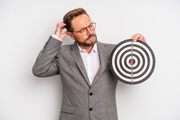 middle age man feeling puzzled and confused, scratching head. target darts concept