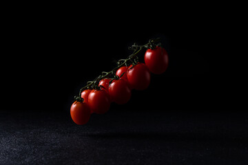 cherry tomatoes on a vect on a dark background hanging above the surface tomatoes in drops of water