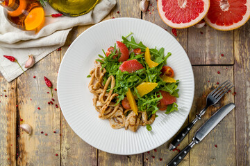 salad with citrus and squid on white plate on wooden table top view