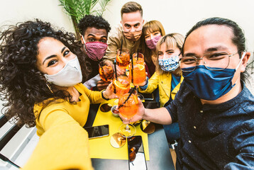 Happy friends wearing protective face masks taking selfie at restaurant - New normal lifestyle...
