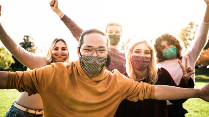 Group of young people wearing face masks having fun outdoors - New normal lifestyle concept with...