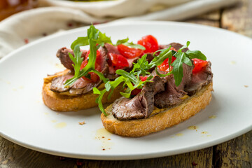 Bruschetta with roast beef, tomatoes and aragula on white plate
