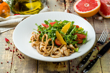 salad with citrus and squid on white plate on wooden table