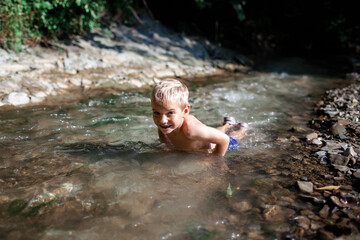 Happy boy swimming in stream canyon river in the mountains, nature pool. Cold water, hardening and natural spa procedure, wildlife and green tourism, summer holidays